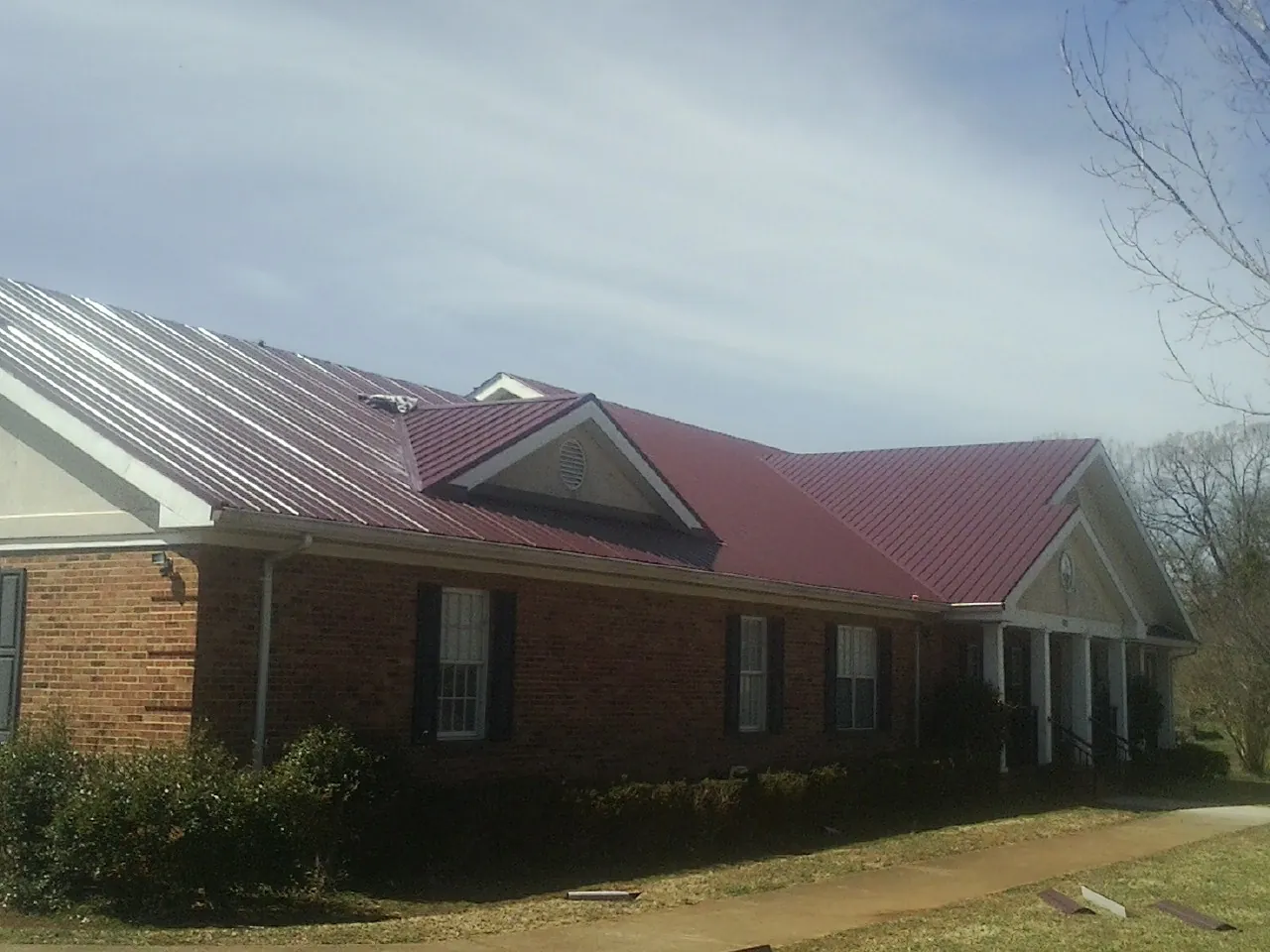 Red metal roof with gabled entries on a long brick building, from a Hail Damage Roof Repair job in Chewelah