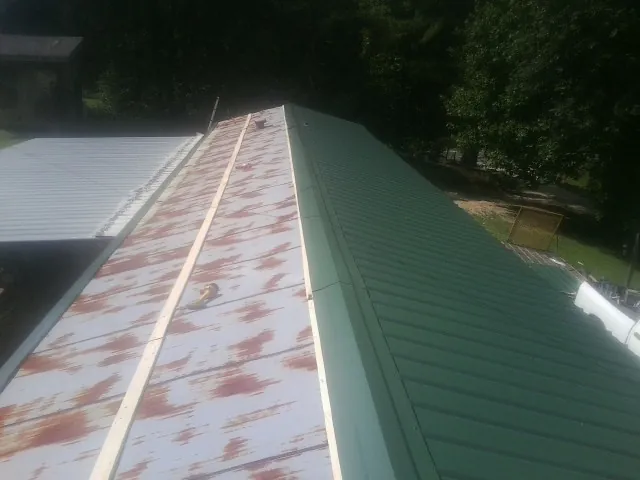 Old rusted panels beside newly installed green metal roofing — Wind Damage Roof Repair by Roofing Brothers in Chewelah