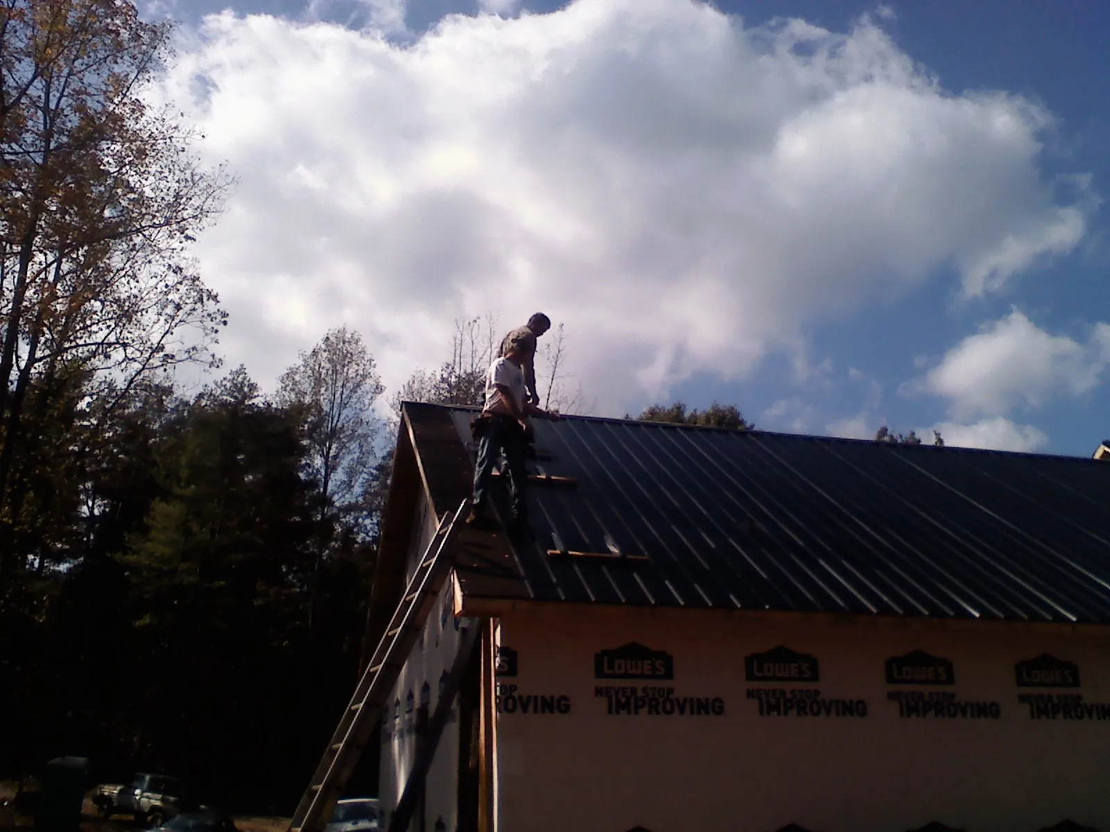 Roofer fastening dark metal panels high against a cloudy sky, from a Roof Inspection job in Chewelah