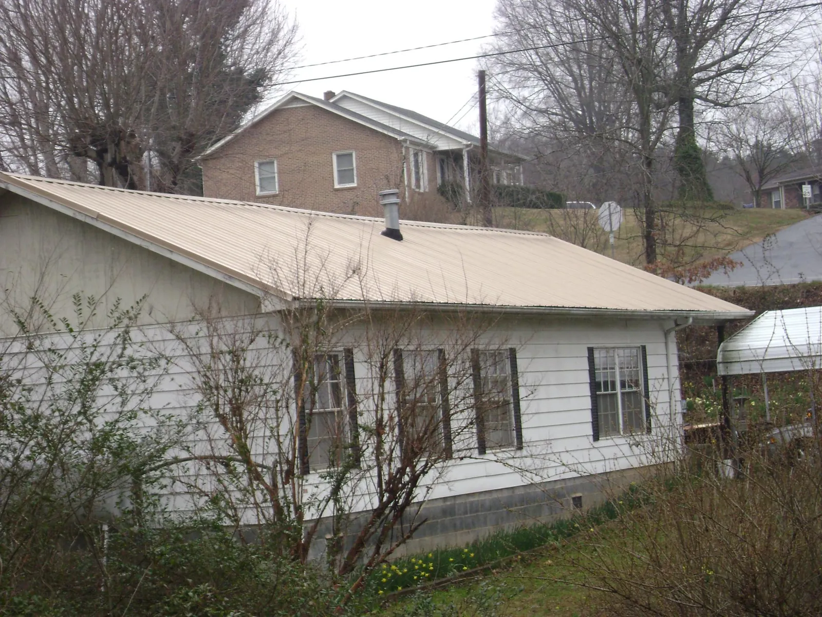 Tan metal roof on a white sided house set into a hillside — Commercial Roofing by Roofing Brothers in Chewelah