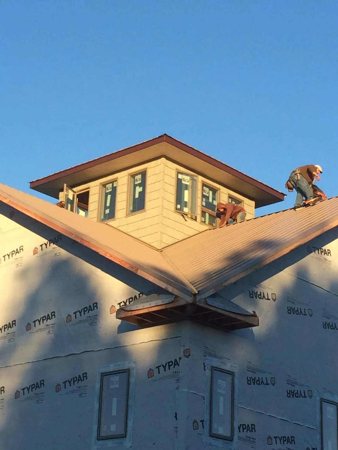 Roofers working around a rooftop cupola on a new metal roof at sunset — Roof Waterproofing in Chewelah by Roofing Brothers